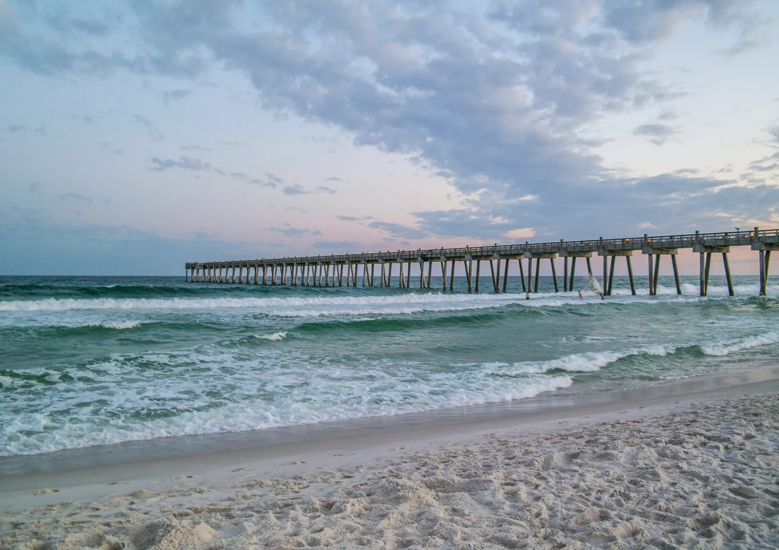 Land near Florida beaches — waves rolling in past a beach pier at dusk